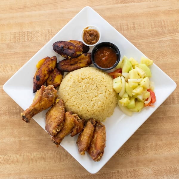 A white rectangular plate holds yellow rice, fried plantains, chicken wings, and a side salad.
