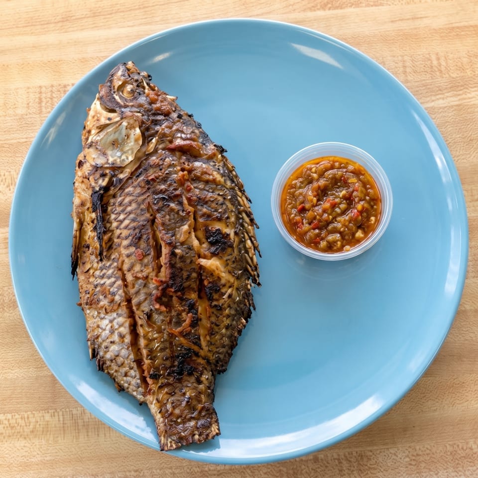 Grilled whole fish with crispy skin and a side of spicy sauce on a blue plate.