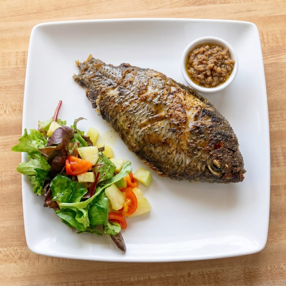 Whole grilled fish with a side salad of greens, tomatoes, and potatoes, and a small bowl of sauce.