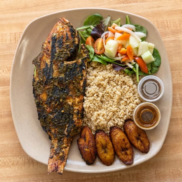 Grilled whole fish with rice, fried plantains, a fresh salad, and two dipping sauces.