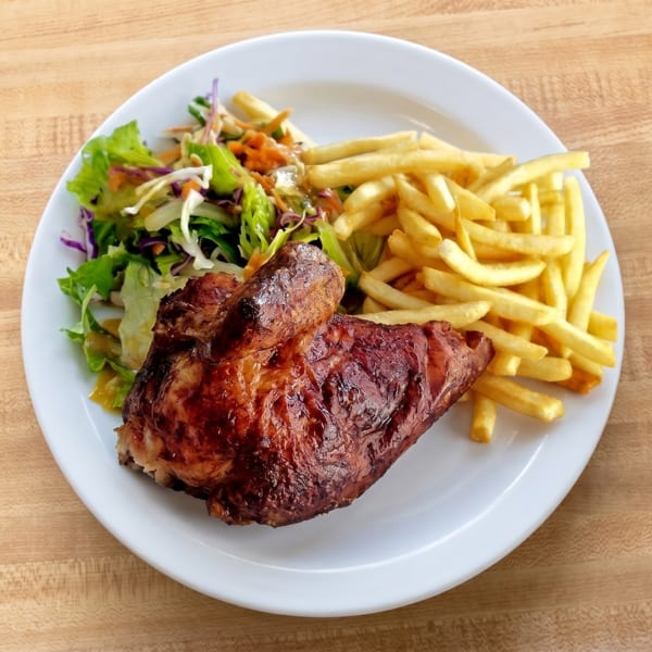 A plate of roasted chicken, golden fries, and a fresh green salad on a wooden table.