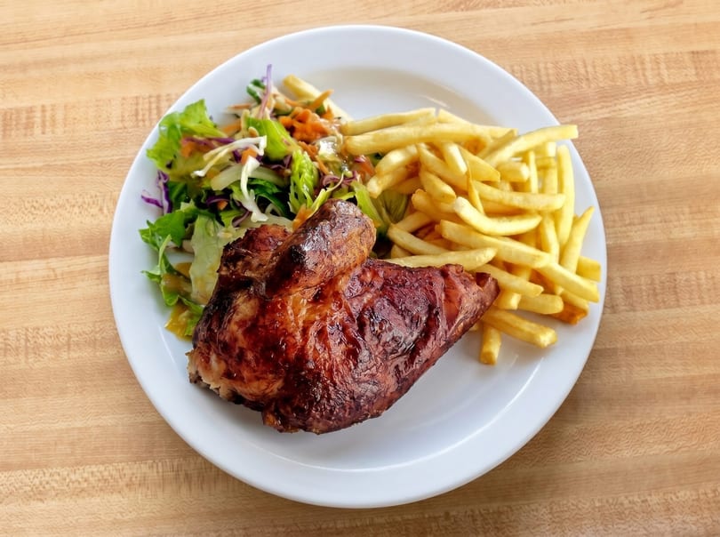 A plate of roasted chicken, french fries, and a side salad on a wooden table.