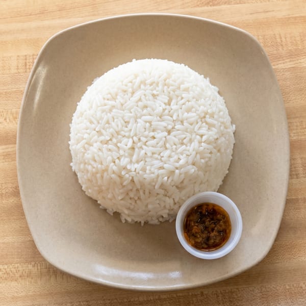 A mound of white rice and a small cup of brown sauce on a beige plate.