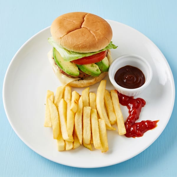 A burger with avocado, lettuce, and tomato, served with fries and ketchup on a white plate.