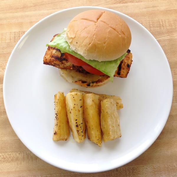 Grilled chicken sandwich with lettuce and tomato, served with seasoned yucca fries on a white plate.