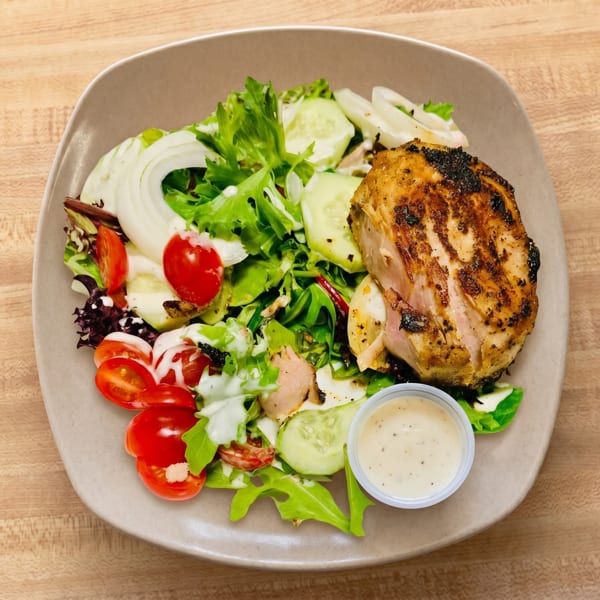 Grilled chicken breast with a fresh garden salad, cherry tomatoes, cucumbers, and dressing on a plate.